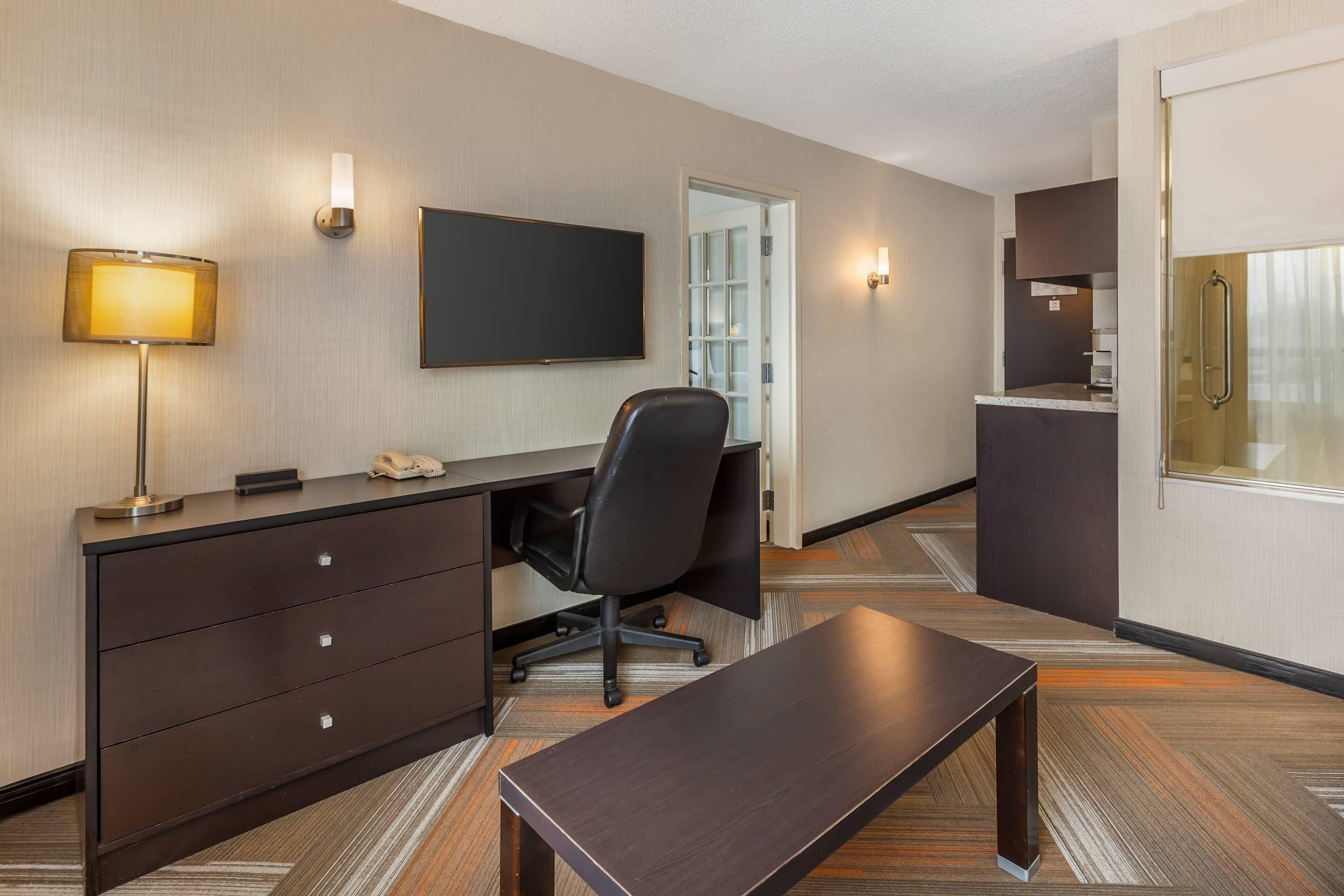 Een hotelkamer met een bureau, stoel, televisie en een kleine kitchenette.