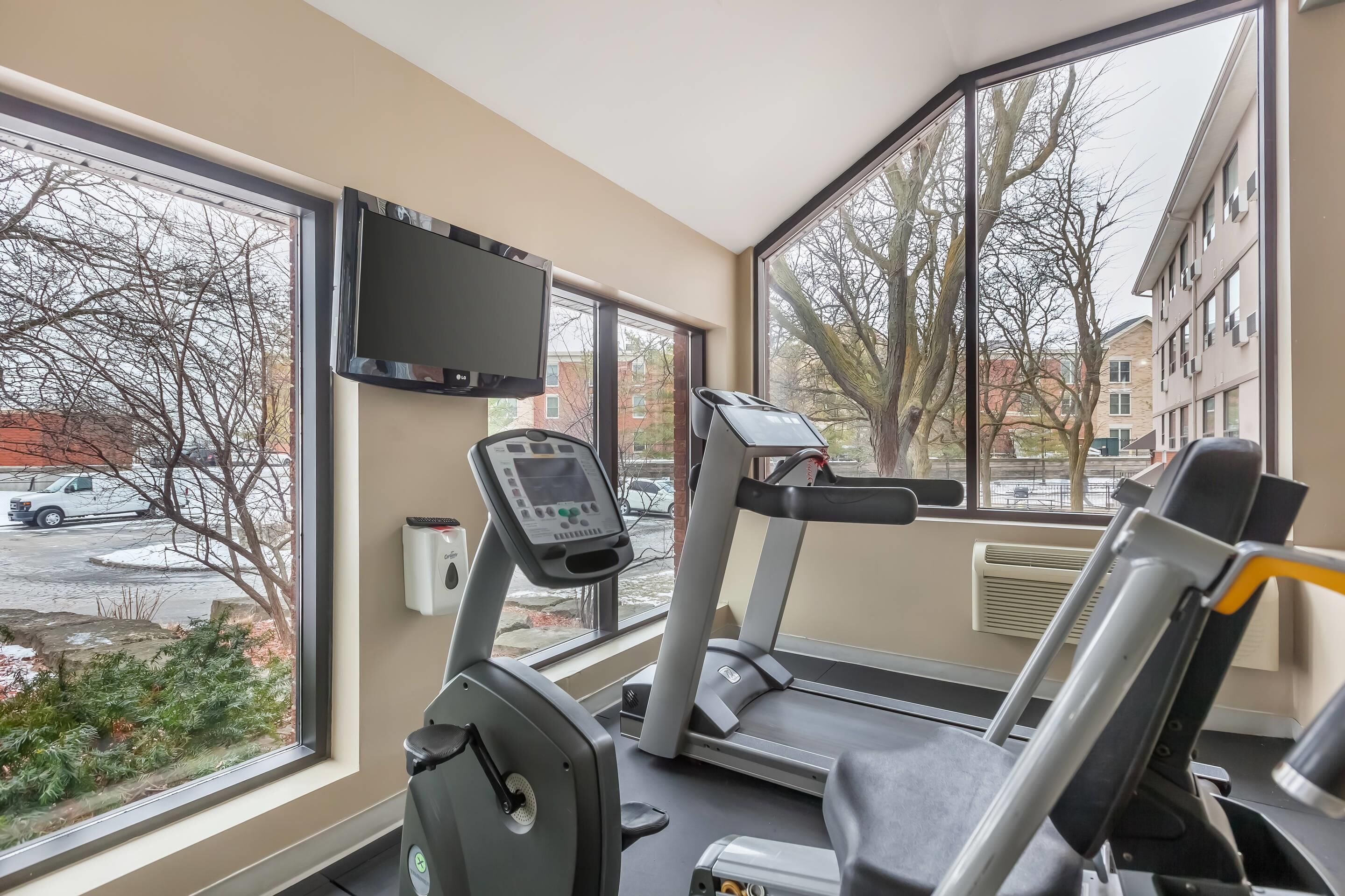 Un gimnasio con cintas de correr, elíptica y un televisor en la pared.