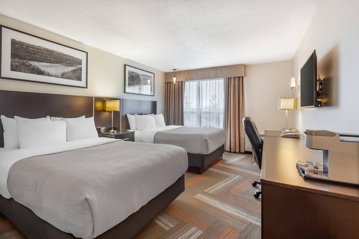 A hotel room with two beds, a desk, a chair, a TV, and two framed pictures on the wall.
