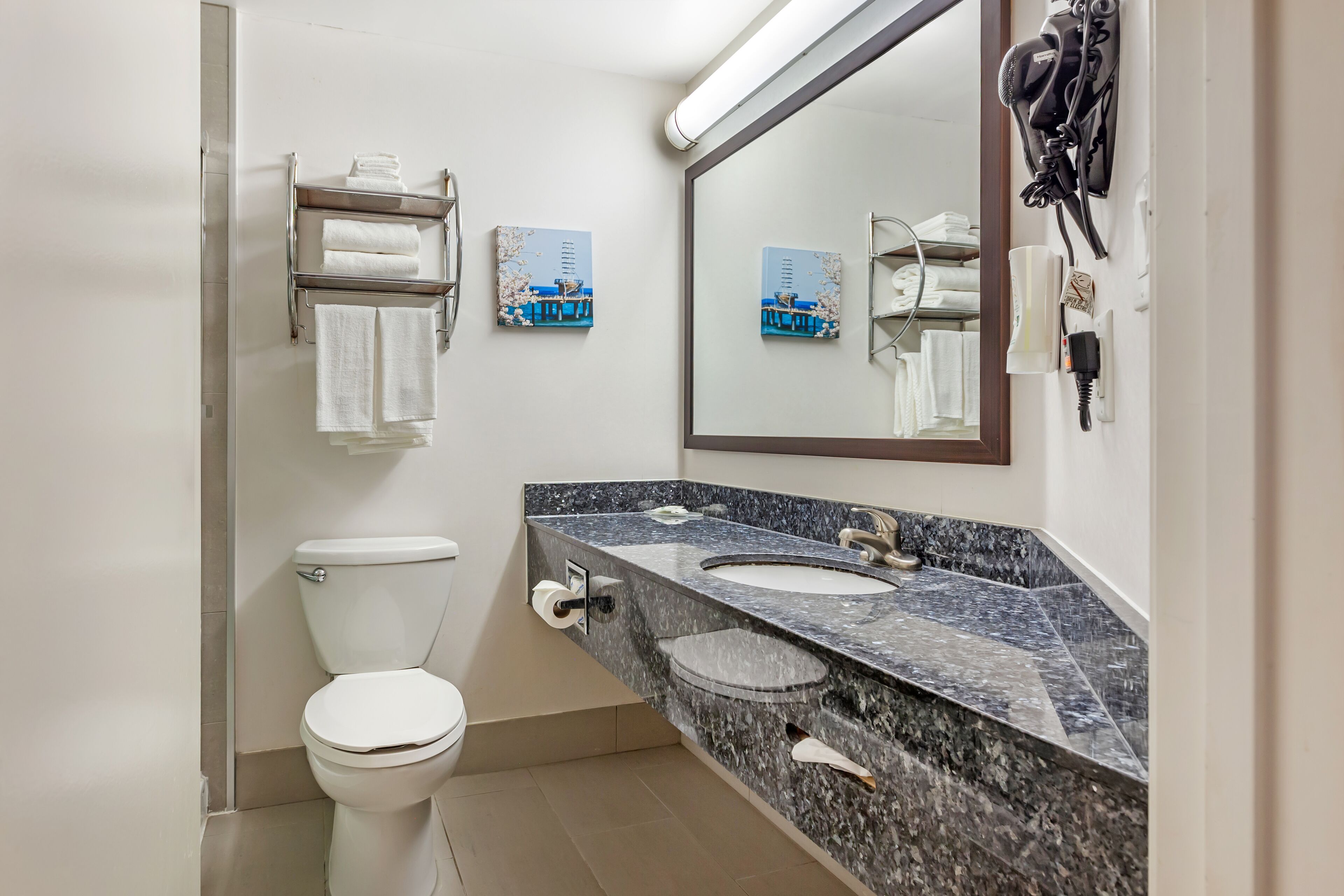 Un baño moderno con inodoro blanco, lavamanos de mármol y dos cuadros enmarcados en la pared.