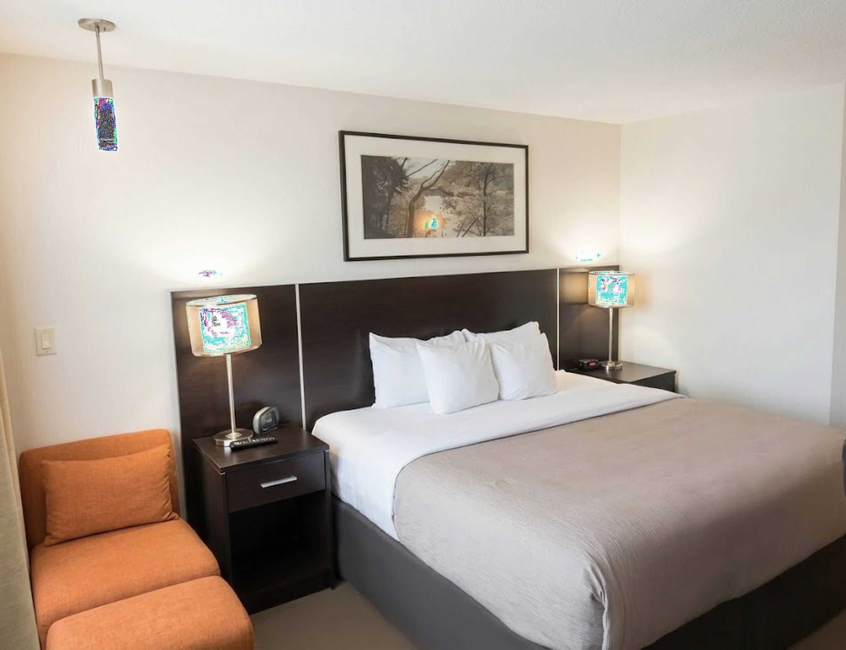 A hotel room with a bed, two bedside tables with lamps, a framed picture on the wall, and a small orange chair.