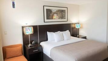 A hotel room with a bed, two bedside tables with lamps, a framed picture on the wall, and a small orange chair.