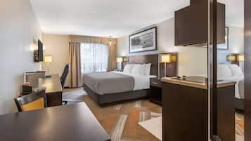 Habitación de hotel con cama, mesitas de noche, escritorio, silla, lámpara, espejo y ventana con cortinas.