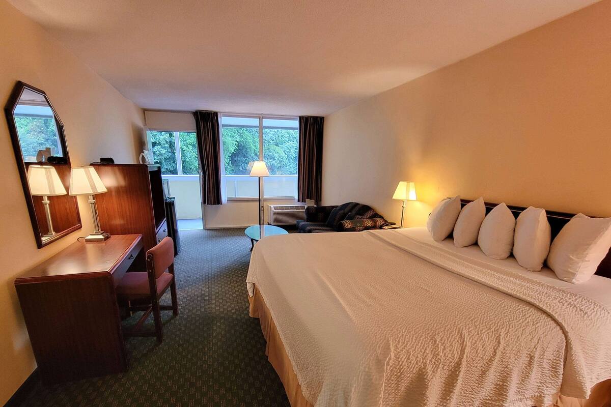 Una habitación de hotel con cama, escritorio, silla y un ventanal amplio.