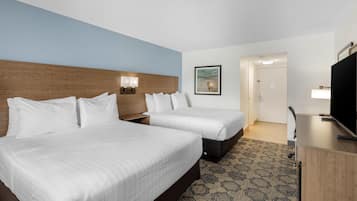 A hotel room with two beds, a wooden headboard, a wall-mounted TV, and a patterned carpet.