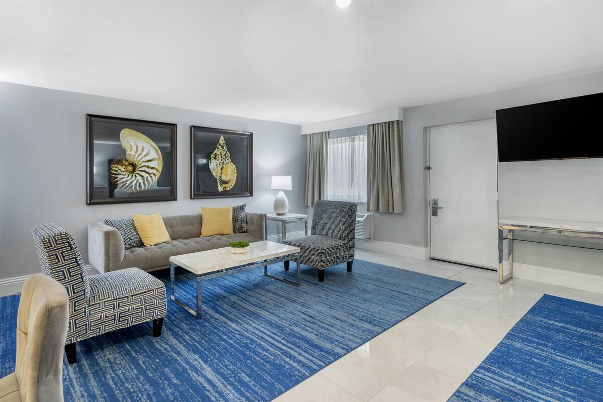 A modern living room with a sofa, two patterned armchairs, a coffee table, and a TV.