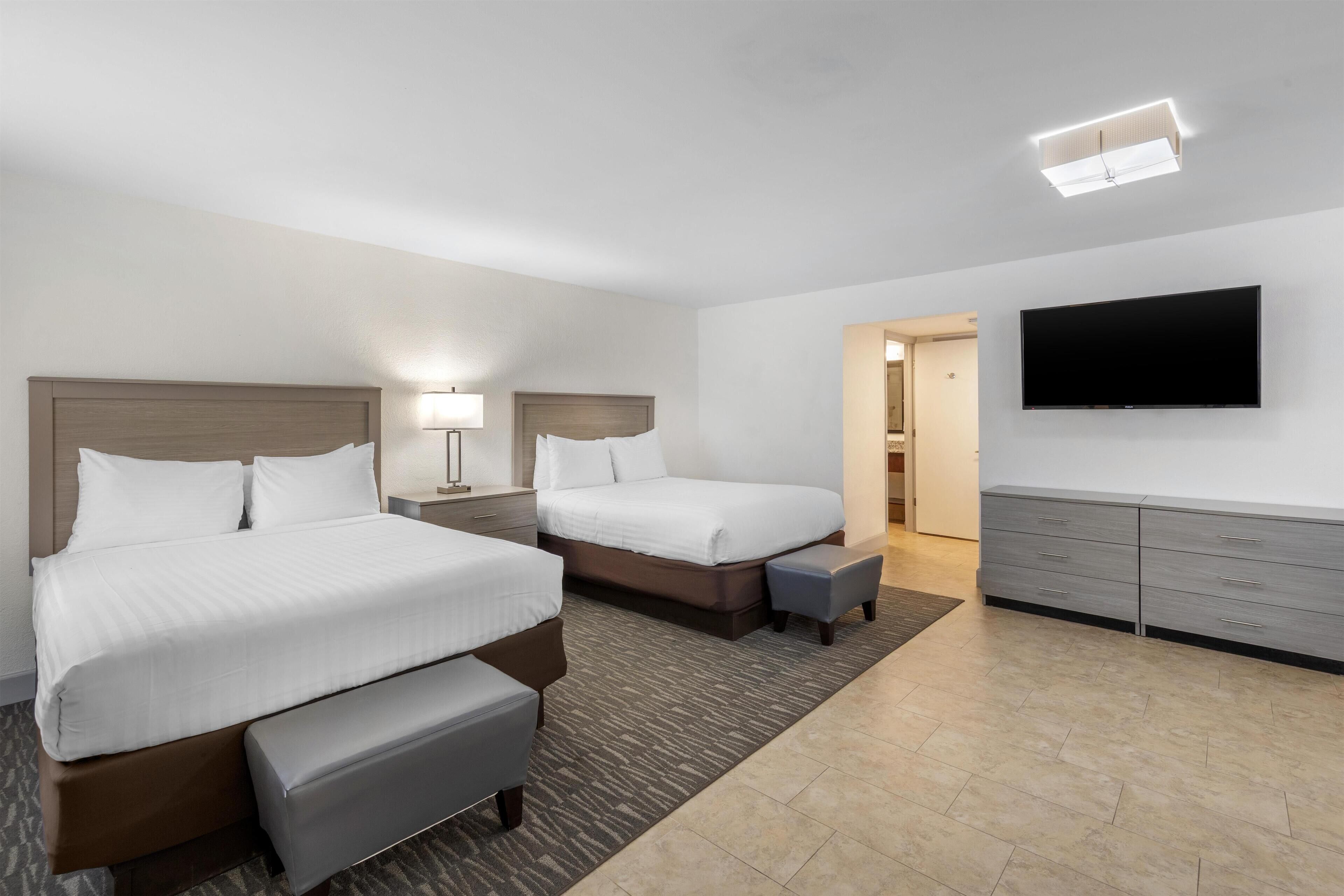 A hotel room with two beds, a flat-screen TV, a desk, and a dresser.