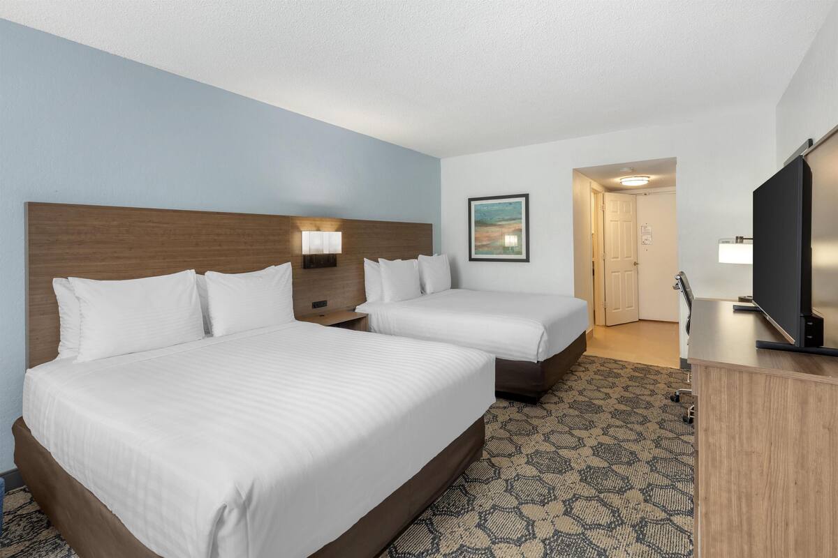 A hotel room with two beds, a desk, a TV, and a painting on the wall.