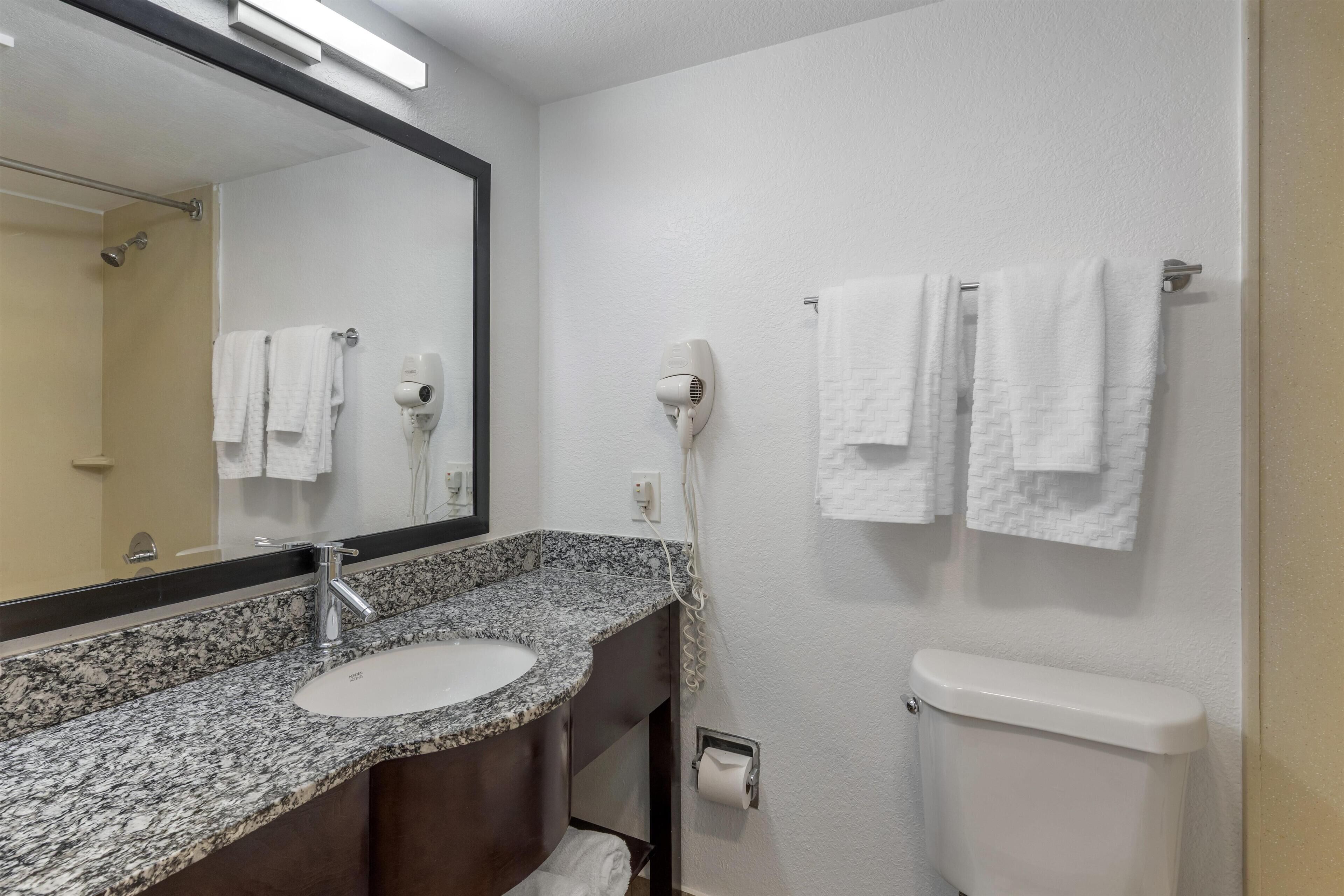 A bathroom with a granite countertop sink, a mirror, a towel rack, a hair dryer, and a toilet.