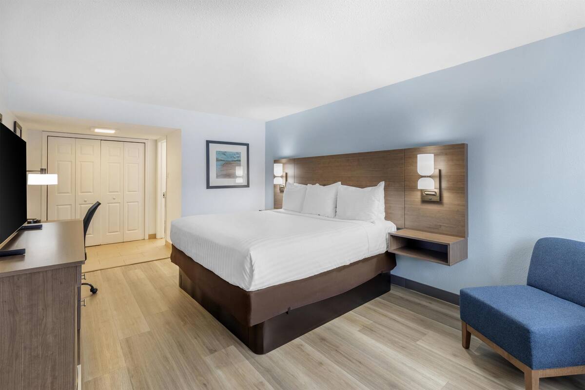 A modern hotel room with a large bed, a desk, a chair, and a TV.