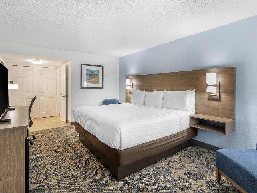 A hotel room with a large bed, a desk, a chair, and a television.