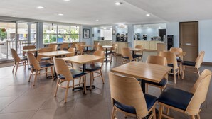 Un vaste espace dédié à la salle à manger, avec des tables et des chaises en bois, un coin café et de grandes fenêtres offrant une vue sur l’extérieur.