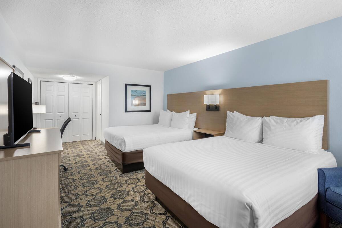 A hotel room with two beds, a desk, a TV, and a patterned carpet.