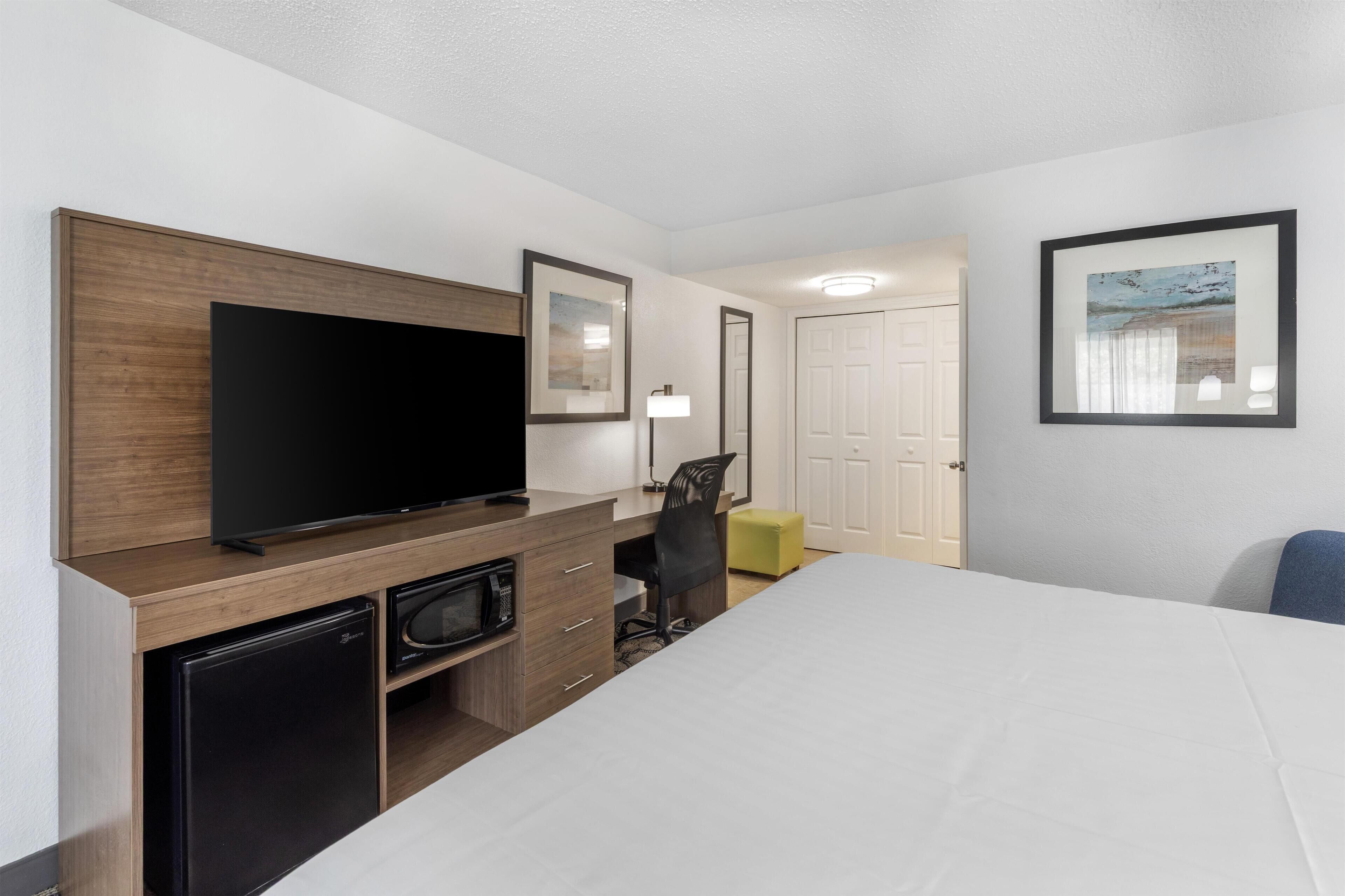 Habitación de hotel con cama, escritorio con televisor, silla, un refrigerador pequeño y una puerta.