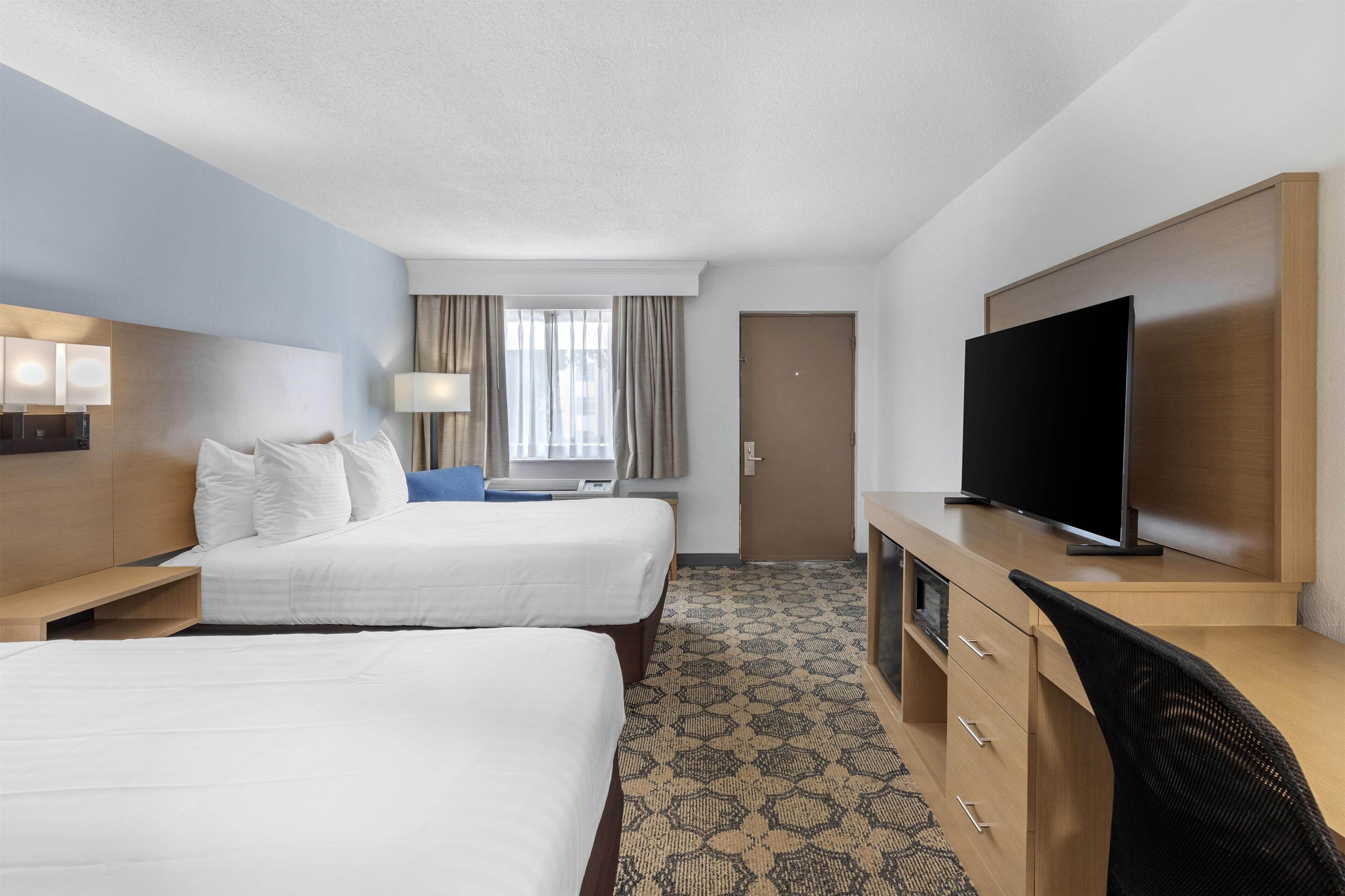 A hotel room with two beds, a desk with a television, a lamp, and a window with curtains.