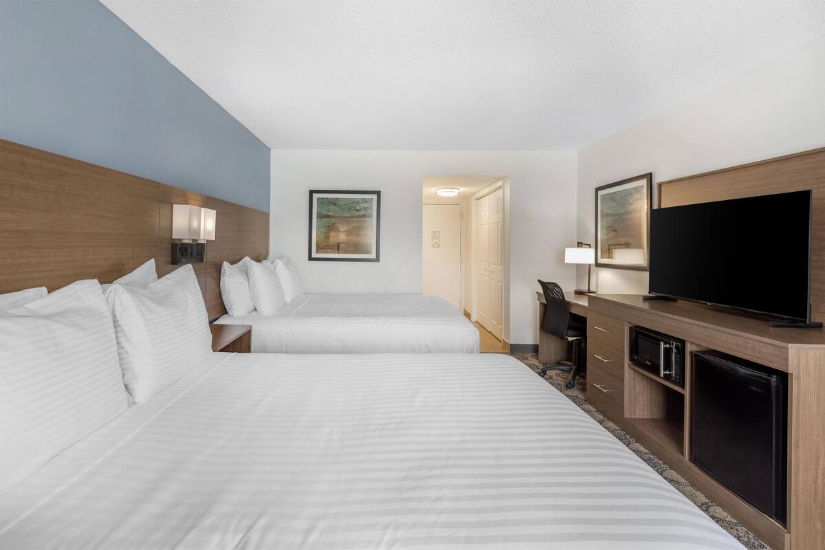A hotel room with two beds, a TV, a desk, and a refrigerator.