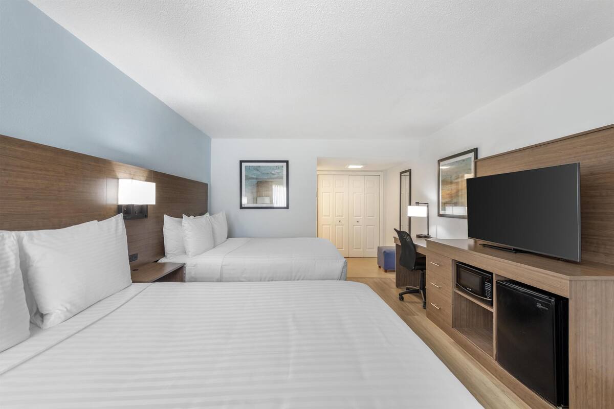 A hotel room with two beds, a TV, a microwave, and a refrigerator.