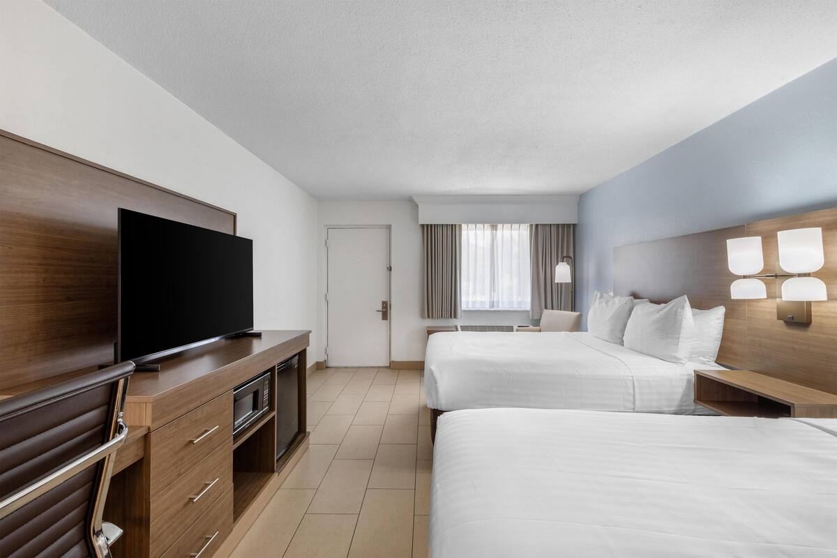 A hotel room with a flat-screen TV, two beds, a wooden dresser, and a nightstand with lamps.