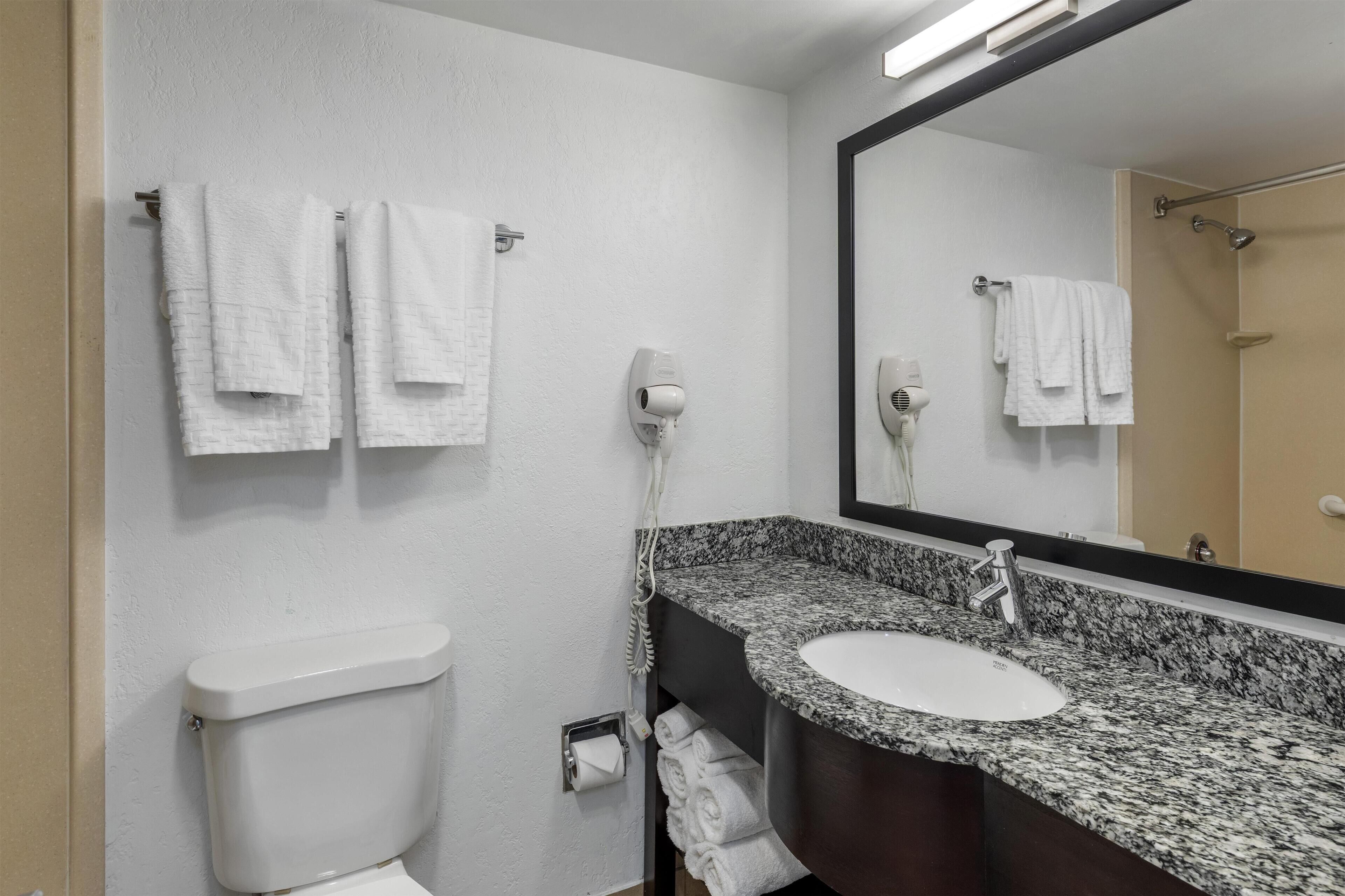 Un baño con inodoro blanco, lavamanos de granito, un espejo y dos toallas colgadas en la pared.
