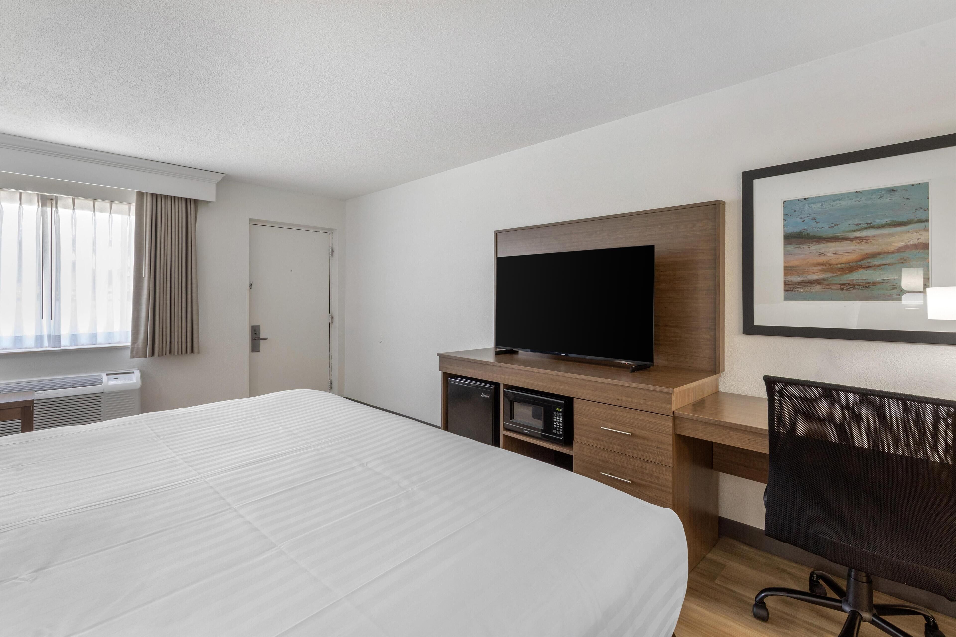 A hotel room with a large bed, a desk with a computer, a television, and a microwave.