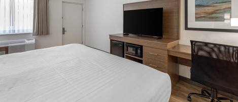 Una habitación de hotel con una cama grande, un escritorio con una computadora, un televisor y un microondas.