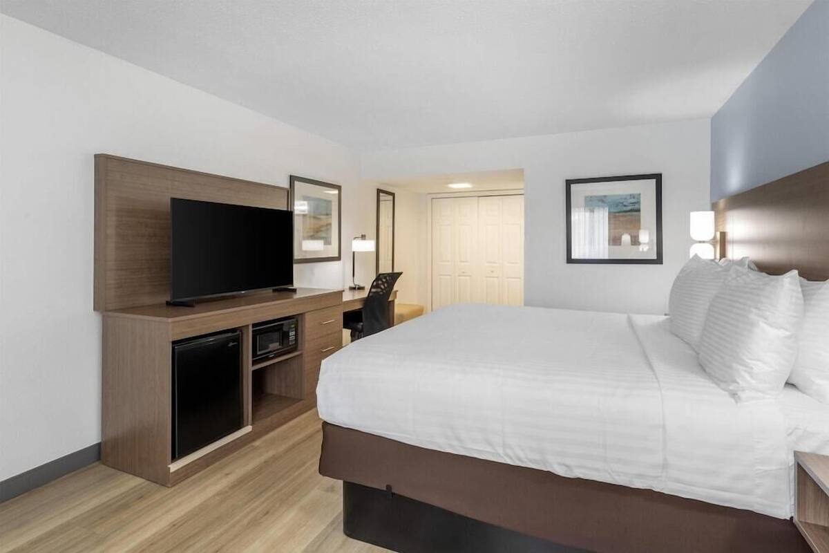 Een hotelkamer met een bed, een televisie, een bureau met een stoel en een kledingkast.
