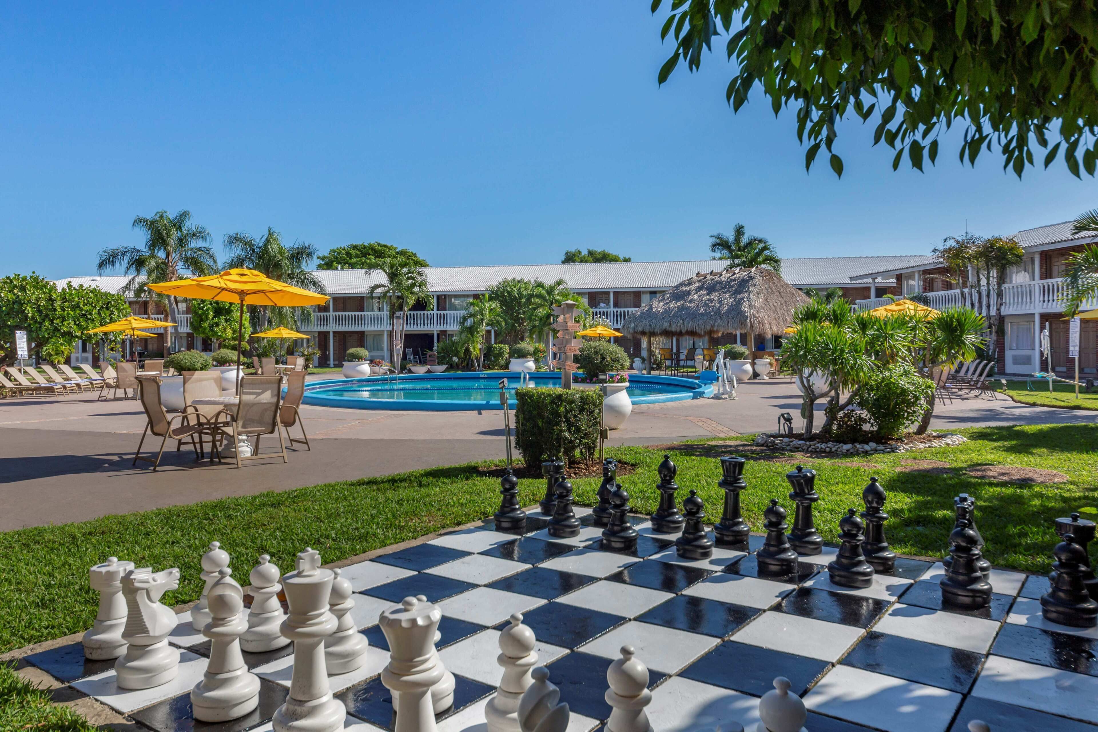 A pool area with a chessboard, outdoor seating, and a building with a thatched roof.