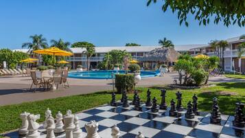 A pool area with a chessboard, outdoor seating, and a building with a thatched roof.