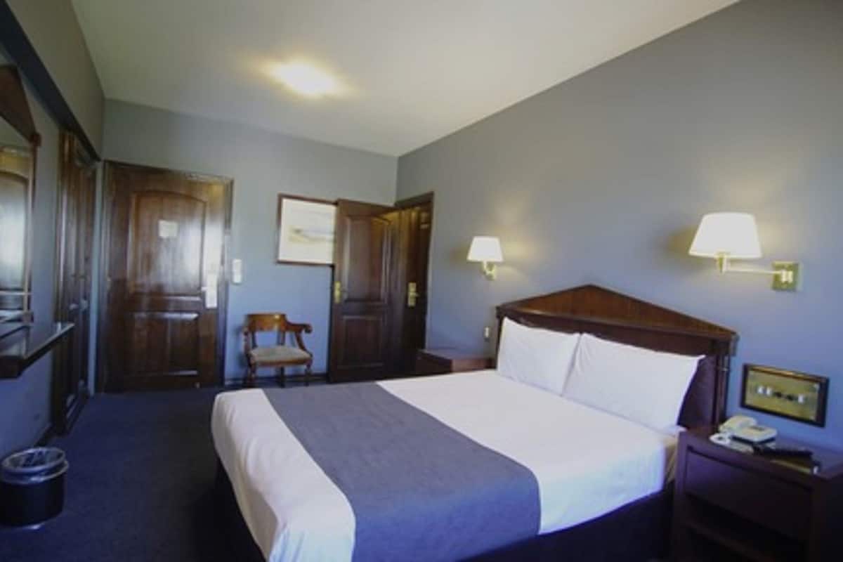 A hotel room with a large bed, two bedside tables, a chair, and a desk.