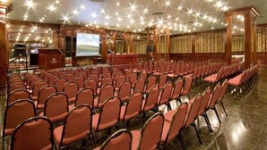 Un salón de conferencias con filas de sillas, un atril y una pantalla grande.