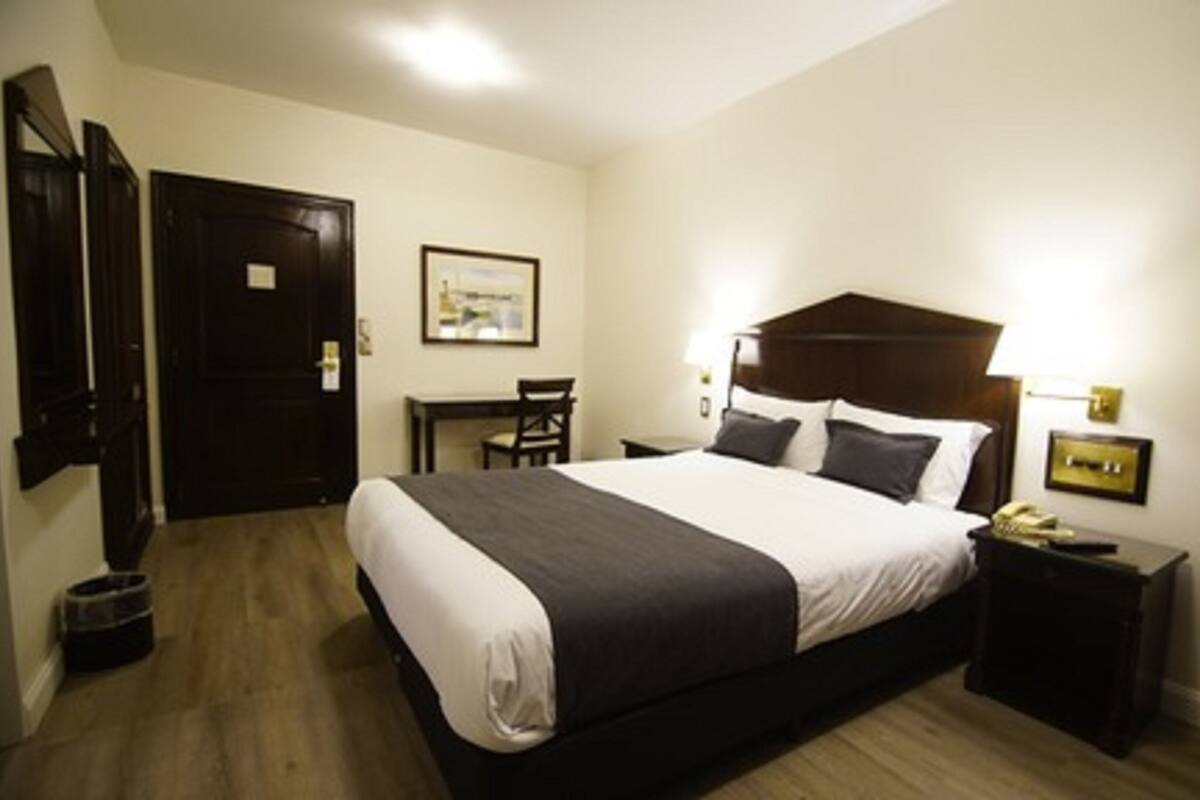 A hotel room with a large bed, a desk, a chair, and a small table.