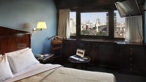 Habitación de hotel con una cama, un escritorio con una computadora portátil, una silla, una lámpara y un televisor.