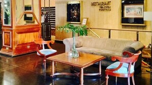 Un vestíbulo con un mostrador de recepción de madera, un sofá, dos sillones, un jarrón con planta y cuadros enmarcados en la pared.
