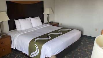 A hotel room with a bed, two bedside tables, a desk with a chair, and a lamp.