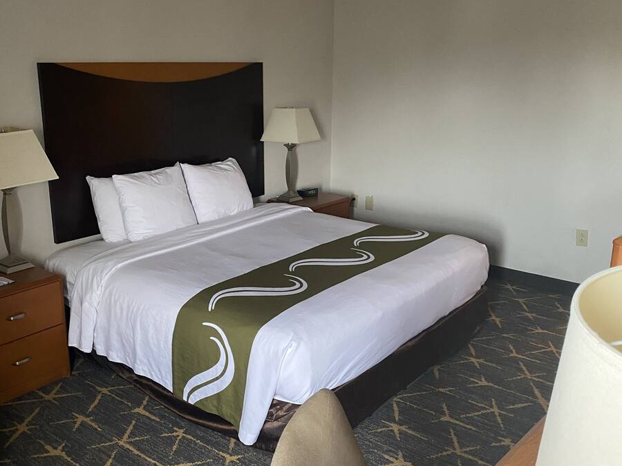 A hotel room with a bed, two bedside tables, a desk with a chair, and a lamp.