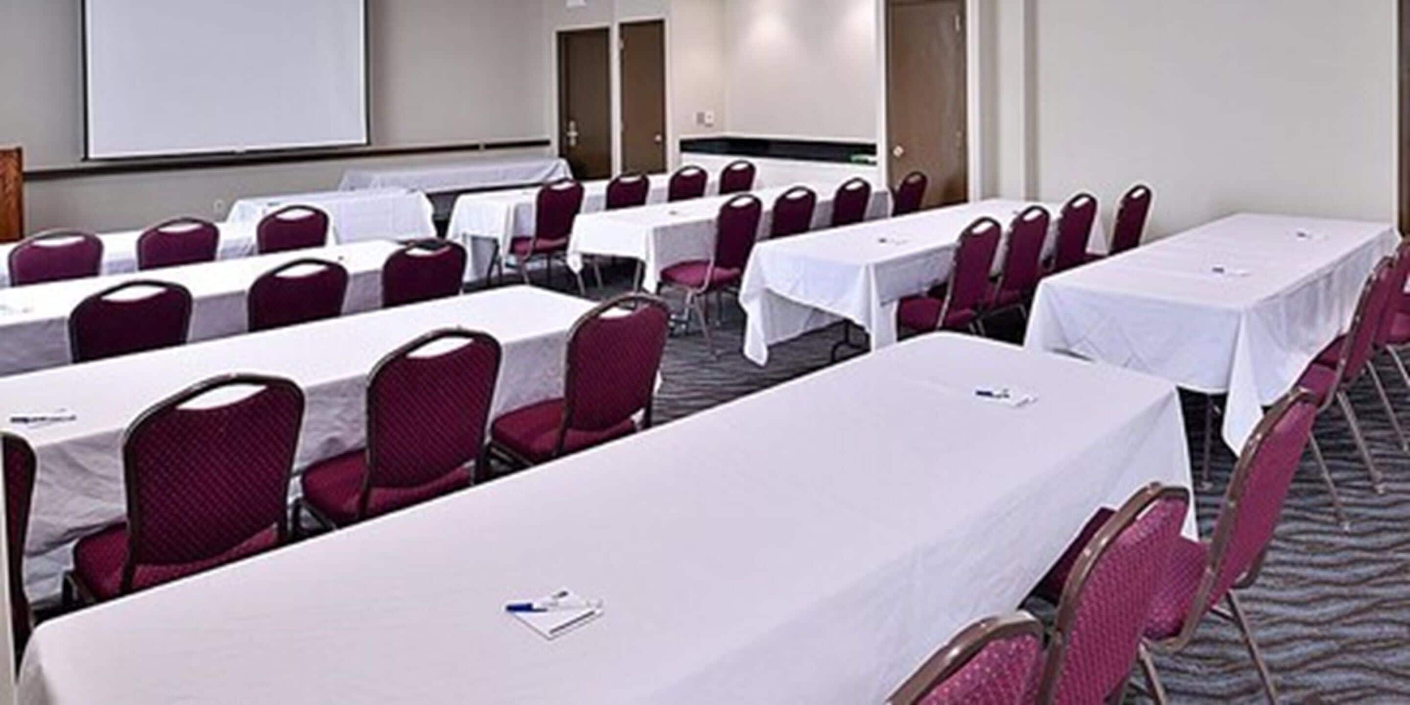 A conference room with multiple tables and chairs, a whiteboard, and a projector screen.
