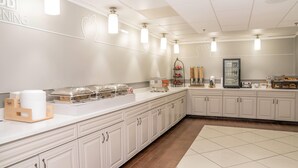 A modern kitchen with white cabinets, a long countertop, and overhead lighting. - Elimwood Hotel, a Ramada by Wyndham (Maryland Heights)