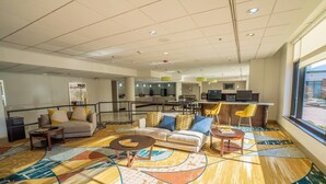 A spacious lobby with a modern design, featuring a large seating area with sofas and chairs, a patterned carpet, and a view of the outside through large windows. - Elimwood Hotel, a Ramada by Wyndham (Maryland Heights)