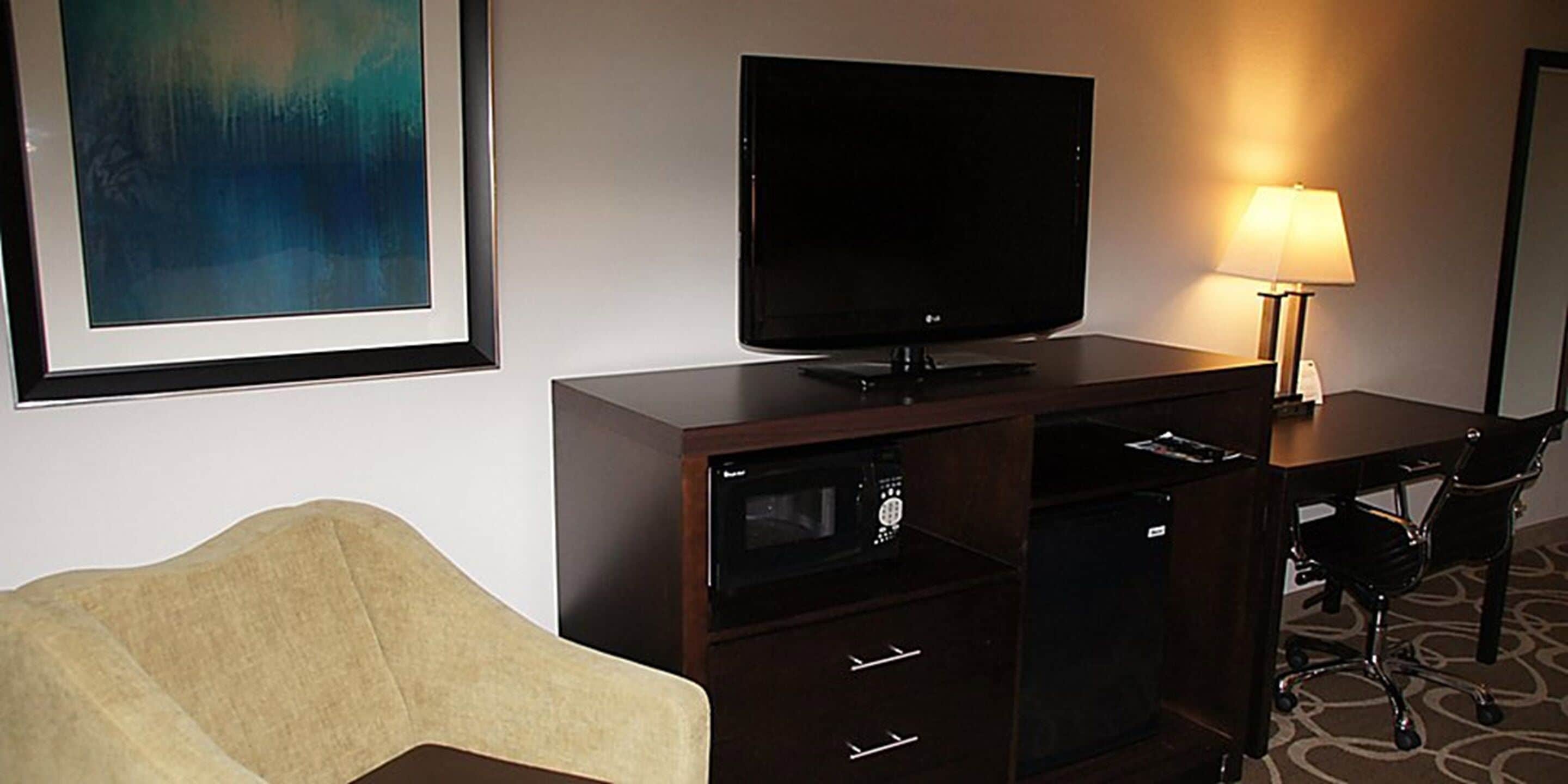 Habitación de hotel con televisión de pantalla plana sobre un mueble de madera, una lámpara, un sofá y un escritorio con una silla.