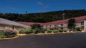 A motel with a red roof, a parking lot, and a forested hillside in the background. - Red Roof Inn Hot Springs (Hot Springs)