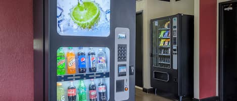 Máquina expendedora con una variedad de bebidas, incluyendo gaseosas y jugos, en un pasillo.