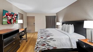 Une chambre d’hôtel avec un grand lit, un bureau avec une chaise, un téléviseur fixé au mur et une fenêtre avec des rideaux.
