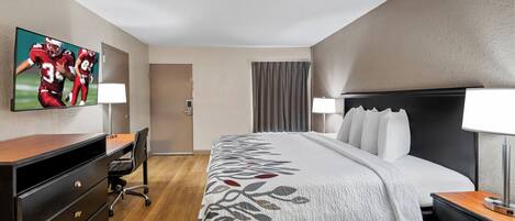 A hotel room with a large bed, a desk with a chair, a TV on the wall, and a window with curtains.