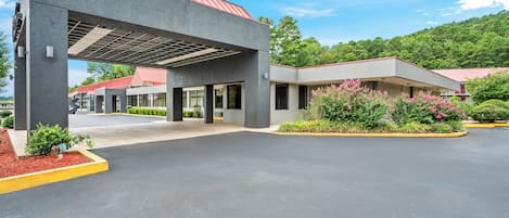 A modern building with a covered entrance, a parking lot, and surrounding greenery.