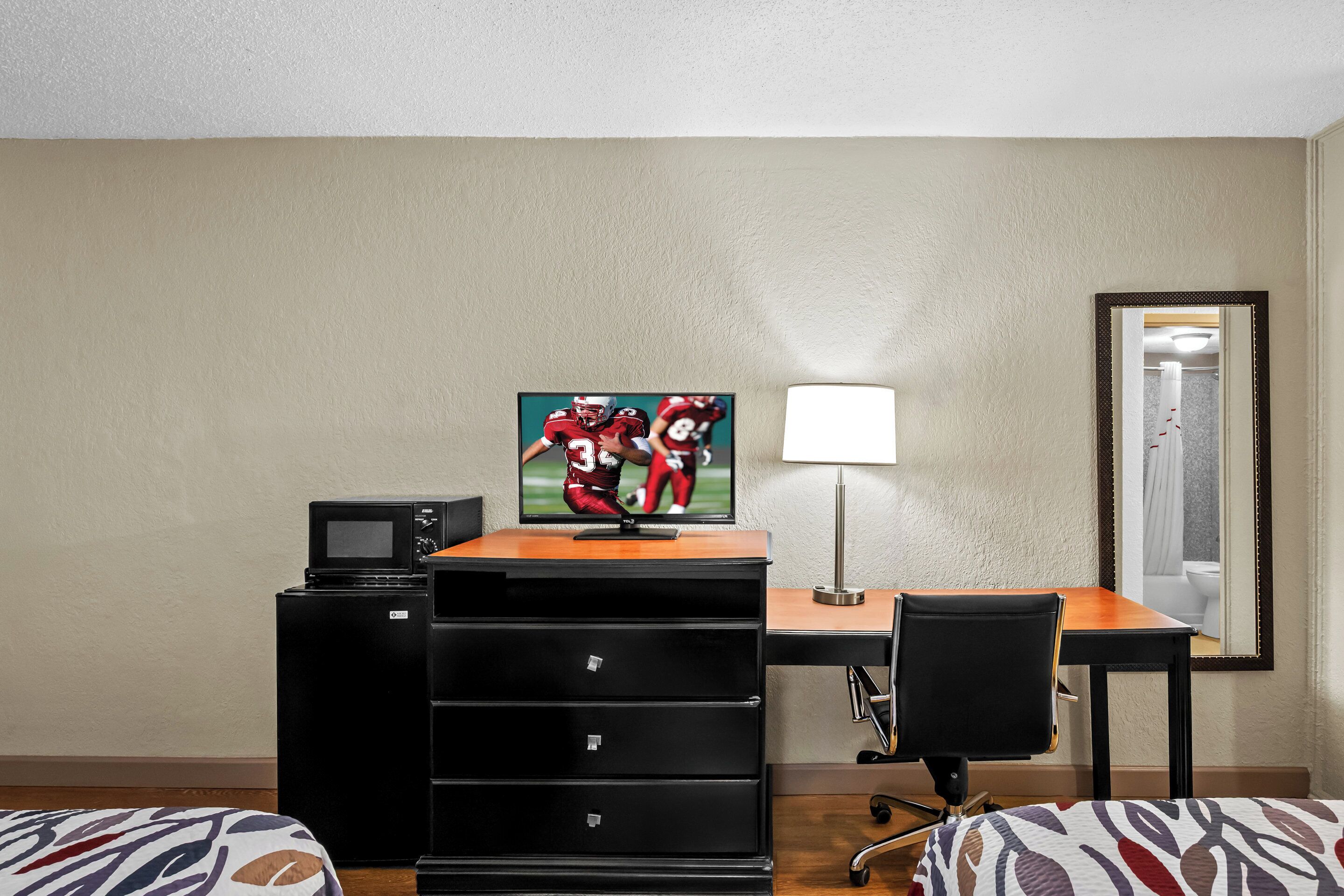 Una habitación de hotel con escritorio, televisión, lámpara, silla y cama.