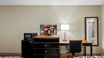 Una habitación de hotel con escritorio, televisión, lámpara, silla y cama.