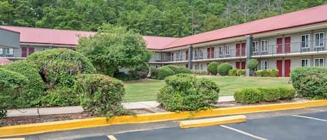 A motel with a red roof, multiple rooms, and a parking lot.