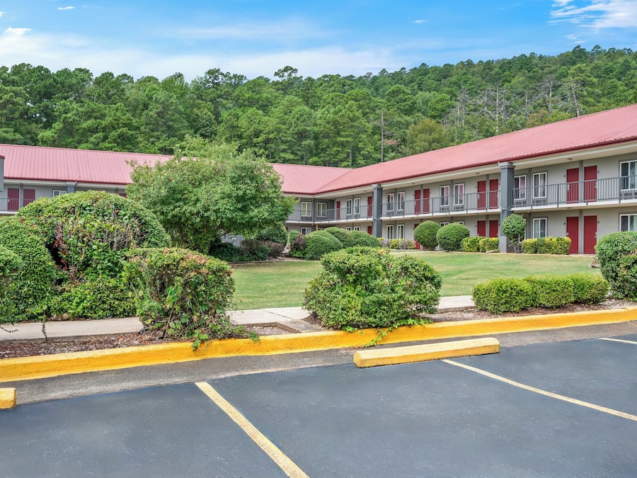 A motel with a red roof, multiple rooms, and a parking lot.