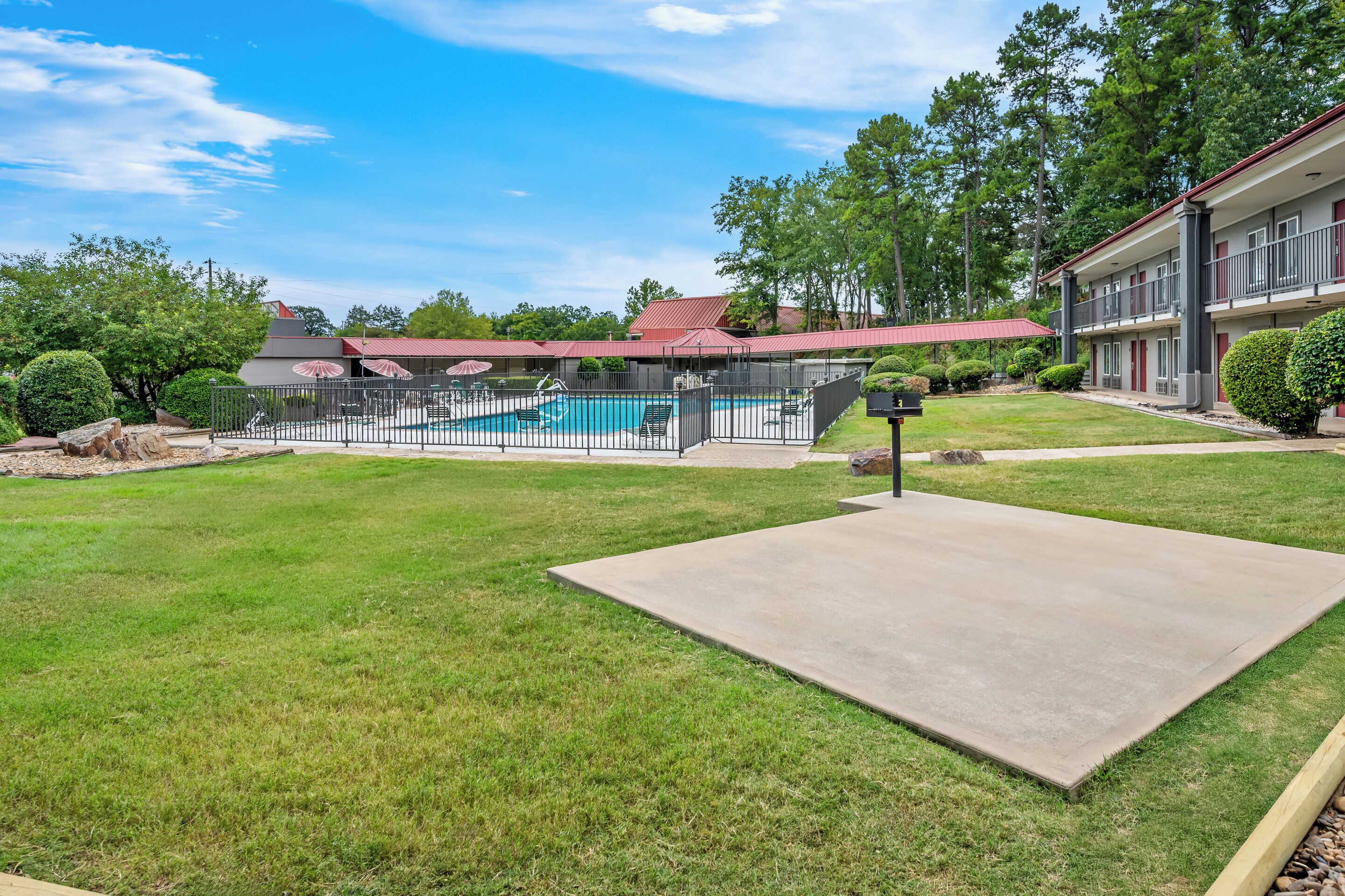 A hotel with a swimming pool, a covered patio, and a well-maintained lawn.