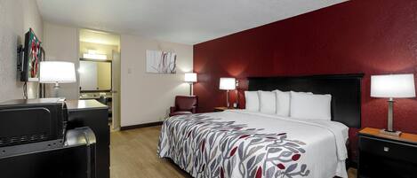 Una habitación de hotel con una cama, dos mesitas de noche con lámparas, un escritorio con una silla, un televisor y un espejo.